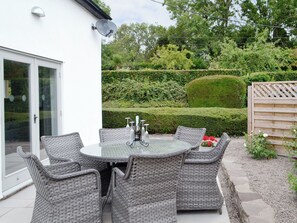 A patio with wicker furniture, a glass table, and a view of a well-maintained garden with hedges. - 2 bedroom accommodation in Grosmont, near Abergavenny (Grosmont, near Abergavenny)