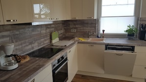 A modern kitchen with a built-in oven, a dishwasher, and a window with blinds. - Blooming vacation home at Scharmützelsee (Wendisch Rietz)