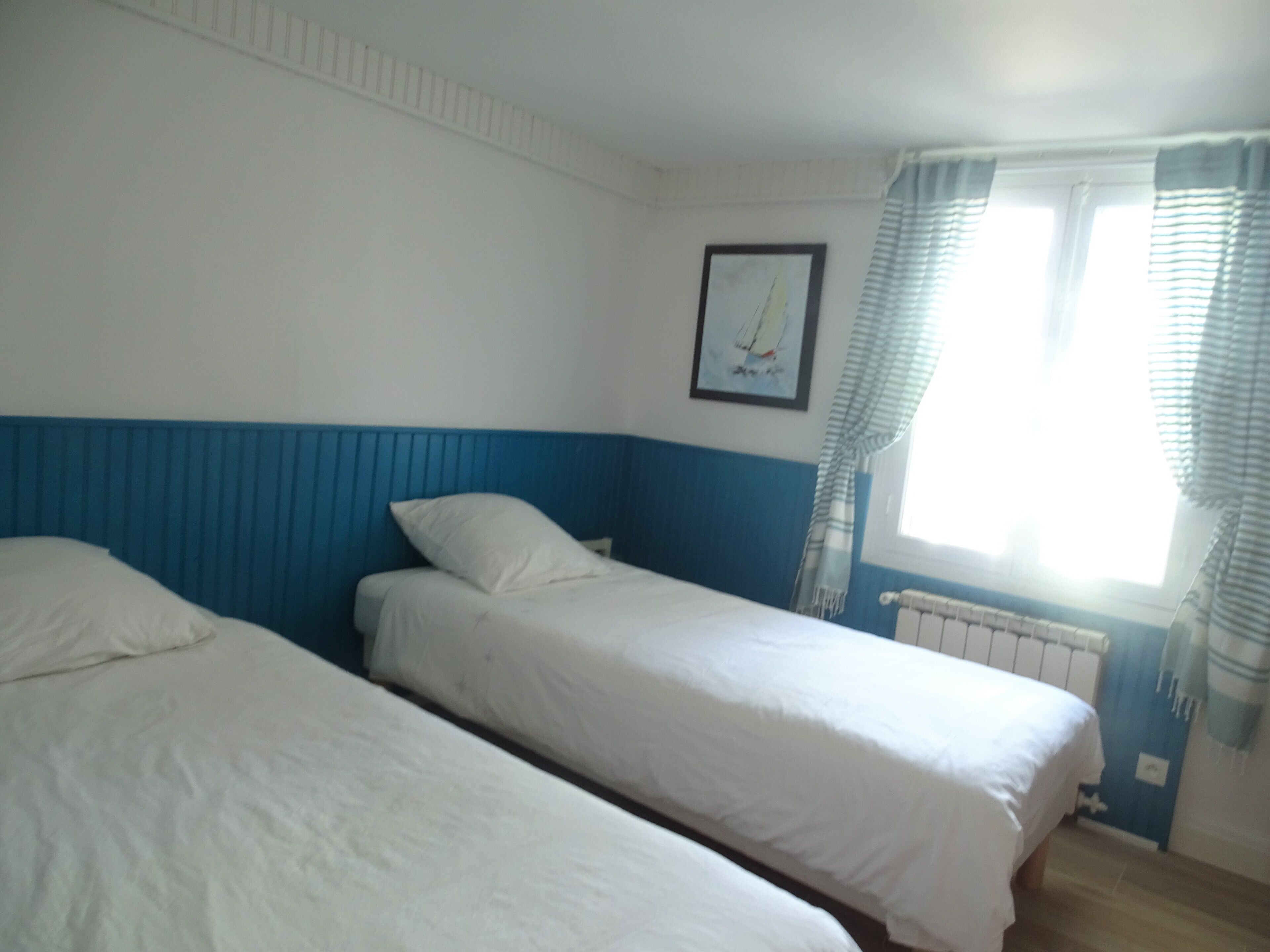 A room with two single beds, a radiator, a framed picture on the wall, and a window with curtains.