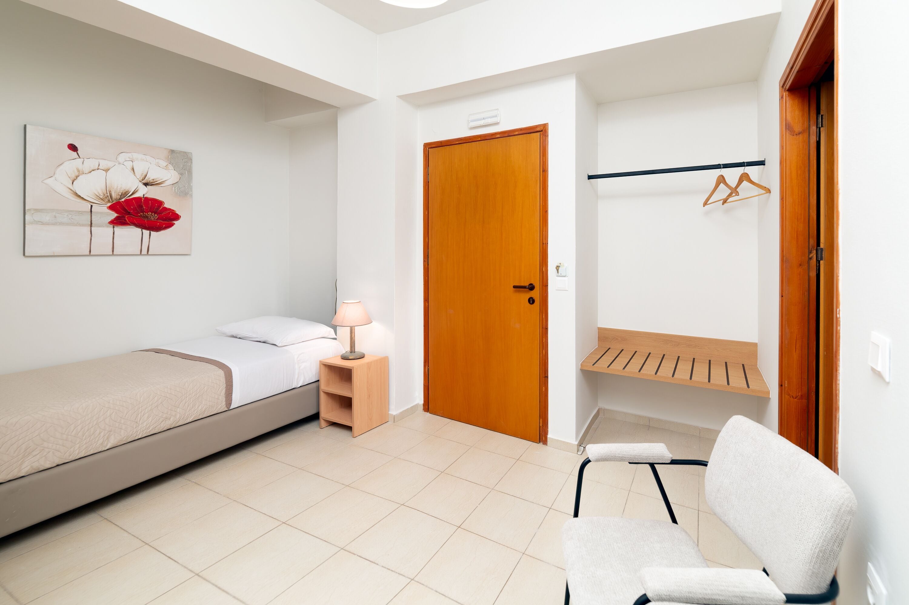 A bedroom with a bed, bedside table, lamp, wooden door, and a wall-mounted coat rack.