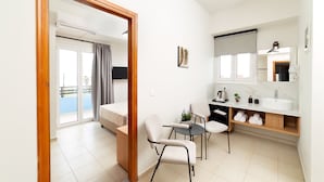 A modern hotel room with a balcony, a small dining area, and a bathroom with a sink and mirror. - Emi Seaside (Malevizi)