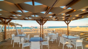 An outdoor dining area with tables and chairs, overlooking a beach. - Emi Seaside (Malevizi)