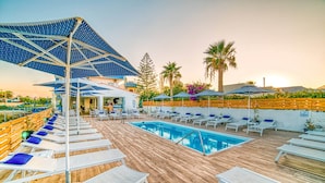 A rooftop pool area with sun loungers and umbrellas, surrounded by wooden decking and palm trees. - Emi Seaside (Malevizi)