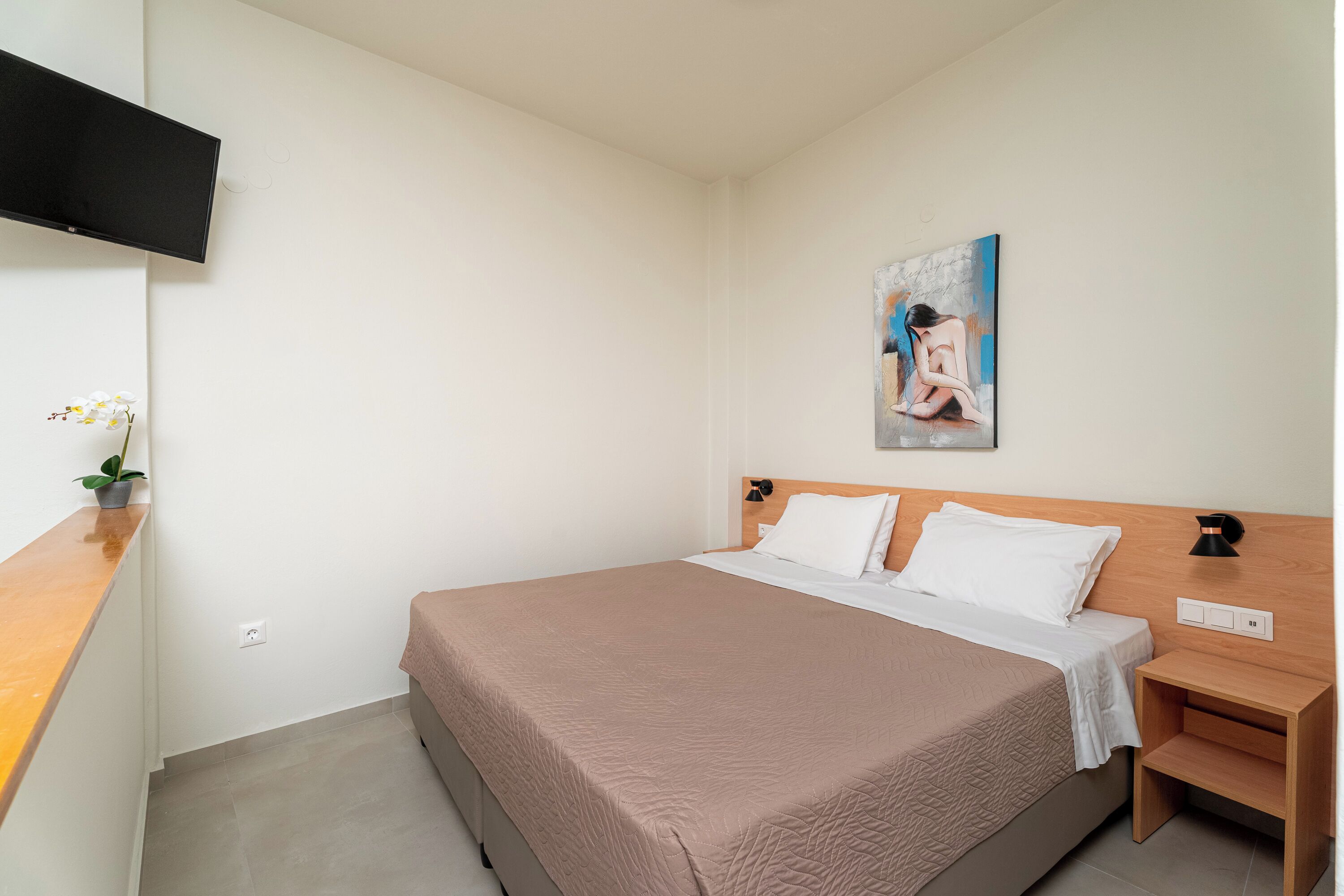 Een slaapkamer met een bed, nachtkastje, tv aan de muur en een schilderij boven het bed.