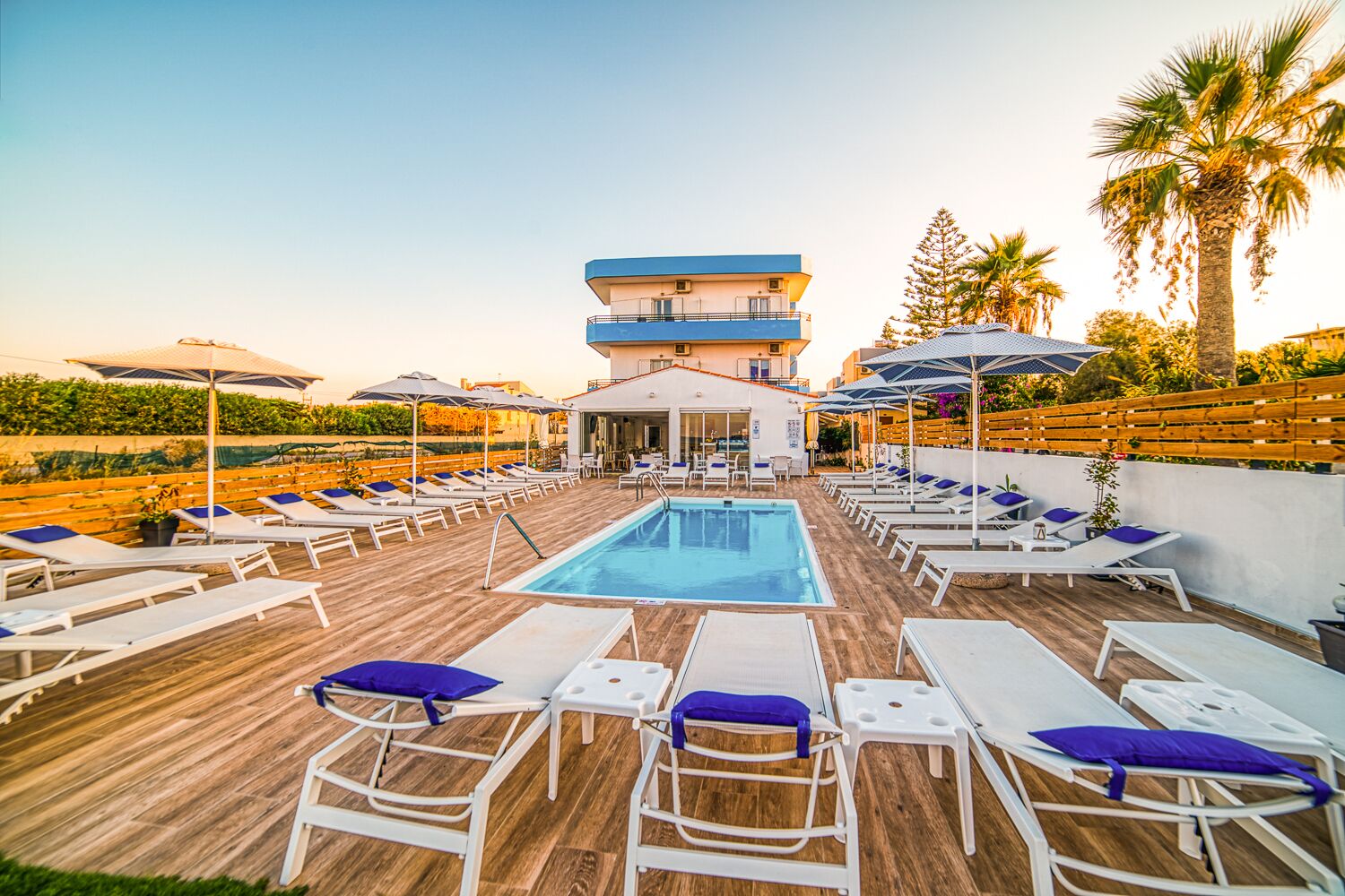 A rooftop pool area with sun loungers, a pool, and a building with a blue and white facade.