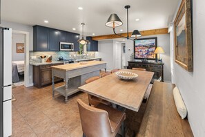 A modern kitchen with dark cabinets, a central island, and a dining area with a wooden table and chairs. - 305 Third Street (Crested Butte)