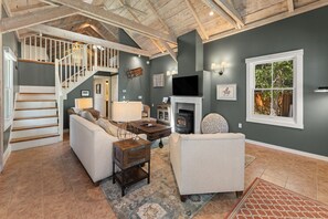 A spacious living room with a fireplace, a staircase, and a large window.