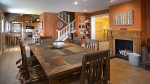 A dining area with a wooden table and chairs, a staircase, a fireplace, and a bookshelf. - 305 Third Street (Crested Butte)