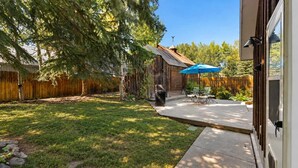 Un jardin avec une terrasse en bois, un barbecue et un parasol bleu.