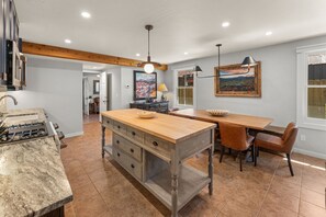 A kitchen with a central island, a dining area with a table and chairs, and a view of the outdoors through a window. - 305 Third Street (Crested Butte)