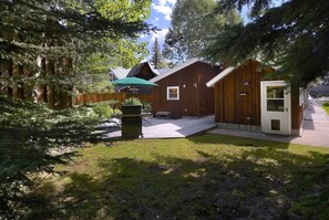 A wooden cabin with a porch, a green umbrella, and a small outdoor seating area.