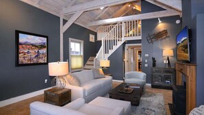 A spacious living room with a high ceiling, a staircase leading to an upper level, a fireplace, and a television. - 305 Third Street (Crested Butte)