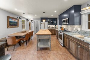 A modern kitchen with dark cabinets, a central island, and a dining area with chairs.