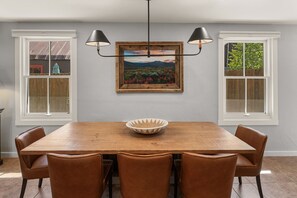 A dining room with a wooden table, six chairs, a central decorative bowl, and two pendant lights.
