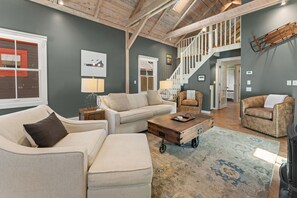 Un salon spacieux avec un plafond haut, un escalier et un coin salon confortable avec une table basse.