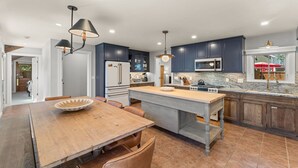 Une cuisine moderne avec des meubles de couleur bleu foncé, un îlot central et un coin repas comprenant une table et des chaises en bois.