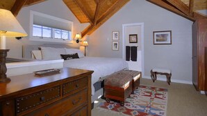 A bedroom with a sloped ceiling, a bed, a dresser, a bench, a chair, and framed pictures on the wall. - 305 Third Street (Crested Butte)