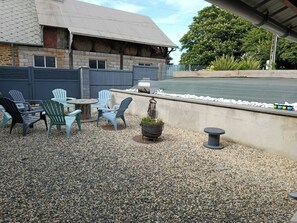 An outdoor patio with Adirondack chairs, a round table, and a potted plant.