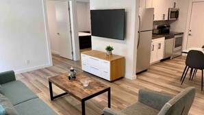 Un salon moderne avec une table basse en bois, deux fauteuils gris et un téléviseur à écran plat fixé au mur.
