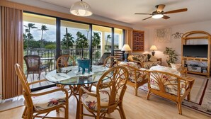Un salón amplio con una mesa de vidrio, muebles de mimbre y un televisor grande.