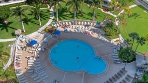 Luchtbeeld van een resort met een centraal gelegen zwembad, ligbedden en palmbomen.