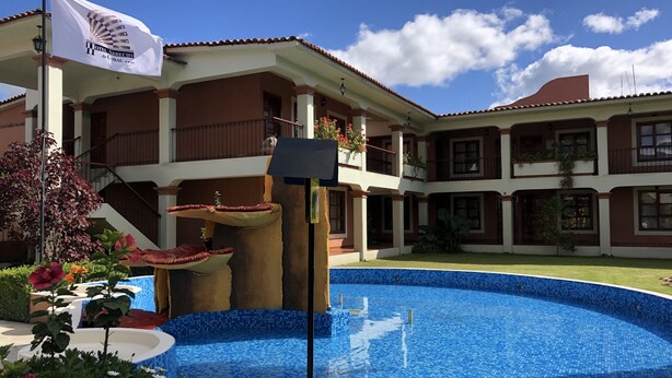 A hotel with a swimming pool, a flag, and a staircase leading to the upper floors. - Hotel Arrecife de Coral (San Cristóbal de las Casas)