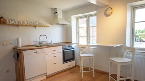Eine Küche mit weißen Schränken, einer Holz Arbeitsplatte, einem Geschirrspüler, einem Backofen und einem Fenster mit Blick auf Grünfläche.