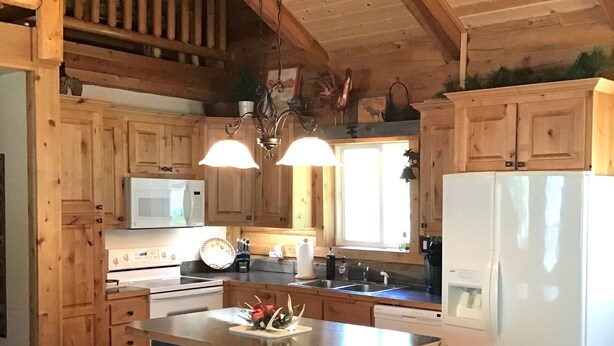 A wooden cabin-style kitchen with a central island, bar stools, and a refrigerator. - Mighty Moose Log Cabin, 20 Minutes to W Yellowstone, Fishing, Sleeps 10. (Island Park)
