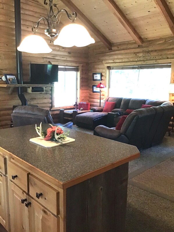 A log cabin interior with a wooden dining area, a sofa, and a television mounted on the wall.