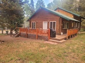 A log cabin with a deck, a covered outdoor seating area, and a staircase leading to the entrance.