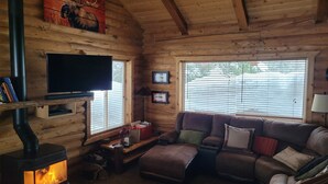 Interior acogedor de una cabaña con chimenea, un sofá, un televisor y paredes de madera.