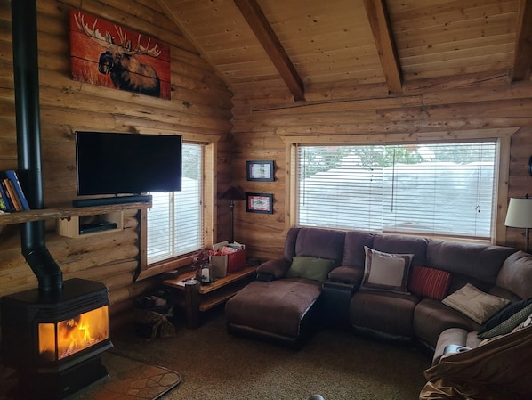A cozy cabin interior with a fireplace, a sofa, a television, and wooden walls. - Mighty Moose Log Cabin, 20 Minutes to W Yellowstone, Fishing, Sleeps 10. (Island Park)