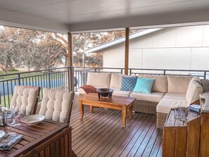 Un espacio al aire libre techado con mesa de madera, sillas y un sofá.