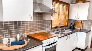 A modern kitchen with white cabinets, a stainless steel range hood, a wooden countertop, and a built-in oven. - Little Beach Bungalow - at Bartletts (Bonny Hills)