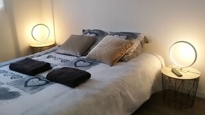 A neatly made bed with a white comforter and heart-patterned pillows, two bedside tables with round mirrors, and a wall-mounted artwork above the bed. - Chambre Avec Douche Privée , Espace Cuisine (Deauville)
