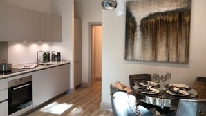 Une cuisine moderne dotée d’appareils électroménagers intégrés, un coin repas avec une table et des chaises en verre, et un grand tableau abstrait accroché au mur.