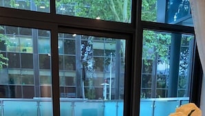 Une chambre moderne avec une table en verre, un vase rempli de fleurs jaunes et une vue sur un jardin grâce à de grandes fenêtres.