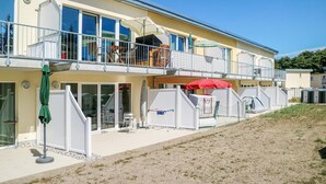 En toetagers bygning med balkon, udendørs siddepladser og et overdækket område med parasoller.