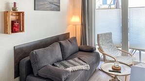 En moderne stue med en grå sofa, et sofabord med et glas og en stol med blomstermønster.