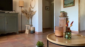 Una sala de estar con televisión, lámpara, un adorno decorativo, un cuadro y una mesa redonda de madera con jarrones.