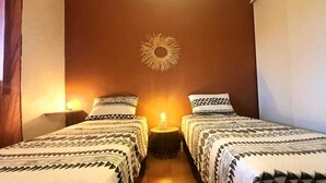 Una habitación con dos camas, un adorno de sol en la pared y una pequeña mesa con una vela.