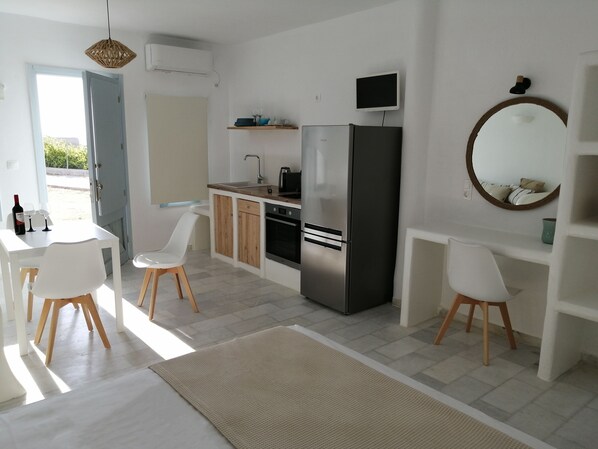 A modern kitchen with white cabinetry, a stainless steel refrigerator, a built-in oven, and a small TV. There is a dining area with white chairs and a table, and a large mirror on the wall. - Two floor cycladic house (Naxos)