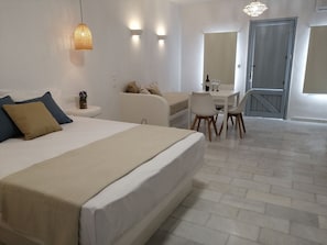 A modern hotel room with a large bed, a dining area, and a door leading to a balcony.