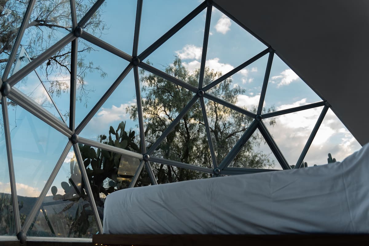 Une pièce dotée d’un plafond en verre aux motifs géométriques, d’un lit et offrant une vue sur les arbres et les montagnes.