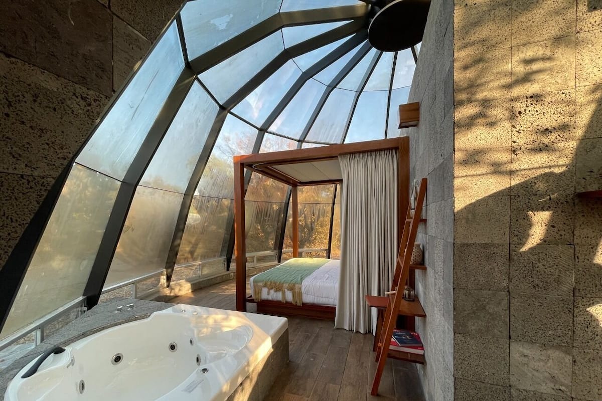 Une chambre avec une grande fenêtre, un lit en bois, une chaise en bois et une baignoire.