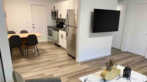 Une cuisine moderne avec des meubles blancs, un téléviseur à écran plat et un coin repas comprenant une table et des chaises.