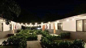 Une cour avec un chemin en briques, bordée de verdure et illuminée par des guirlandes lumineuses.
