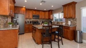Una cocina con armarios de madera, encimeras de granito, un refrigerador de acero inoxidable, un microondas y una estufa a gas.