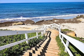 A wooden staircase leading to a beach with white railings and a view of the ocean.