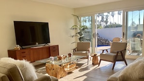 Un salon moderne doté d’un téléviseur à écran plat, de canapés confortables, d’une table basse en verre et offrant une vue sur l’extérieur grâce à de grandes portes-fenêtres coulissantes.